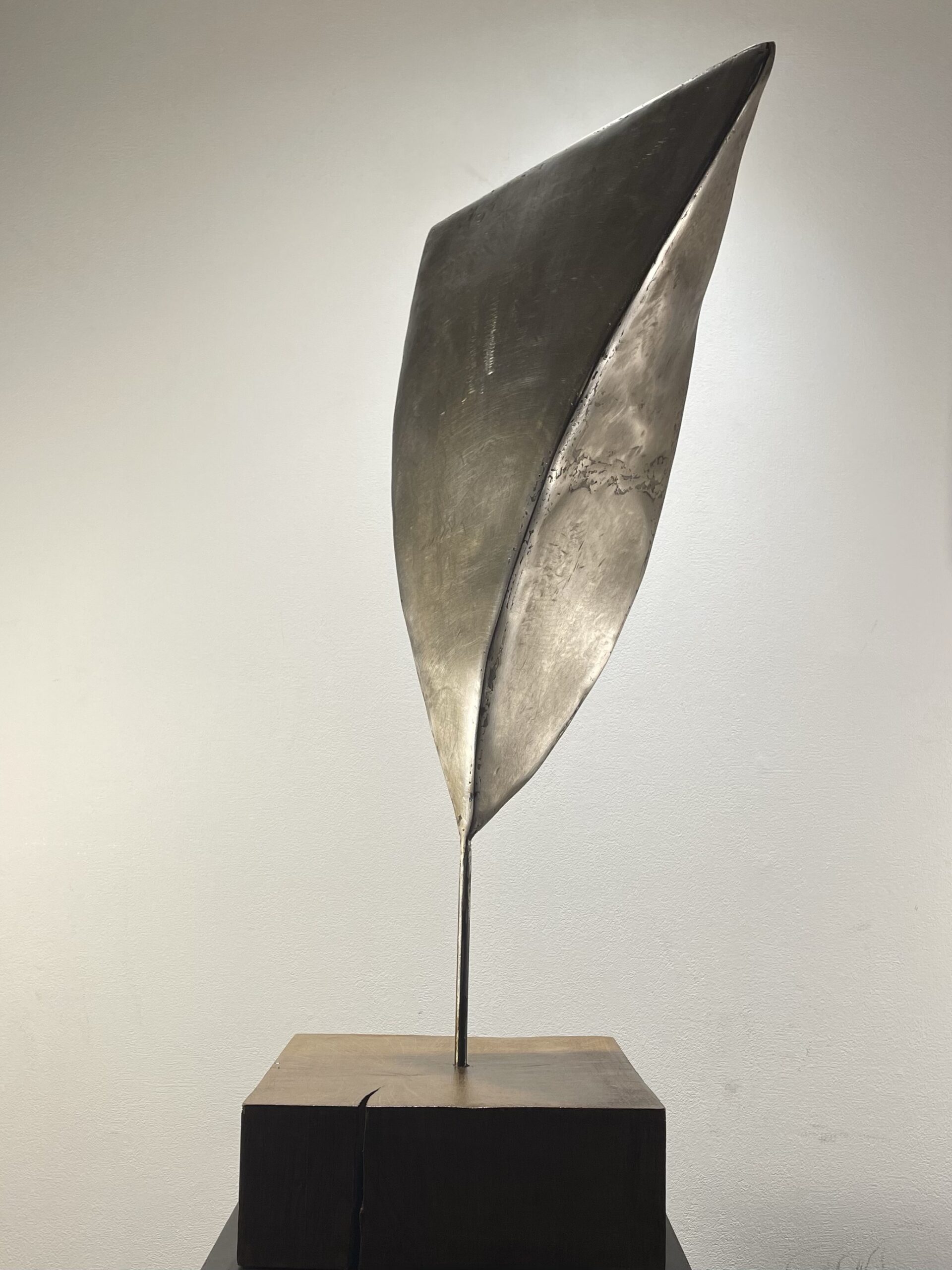 Curved steel sculpture on wood base suggesting bird flight movement with raw industrial texture