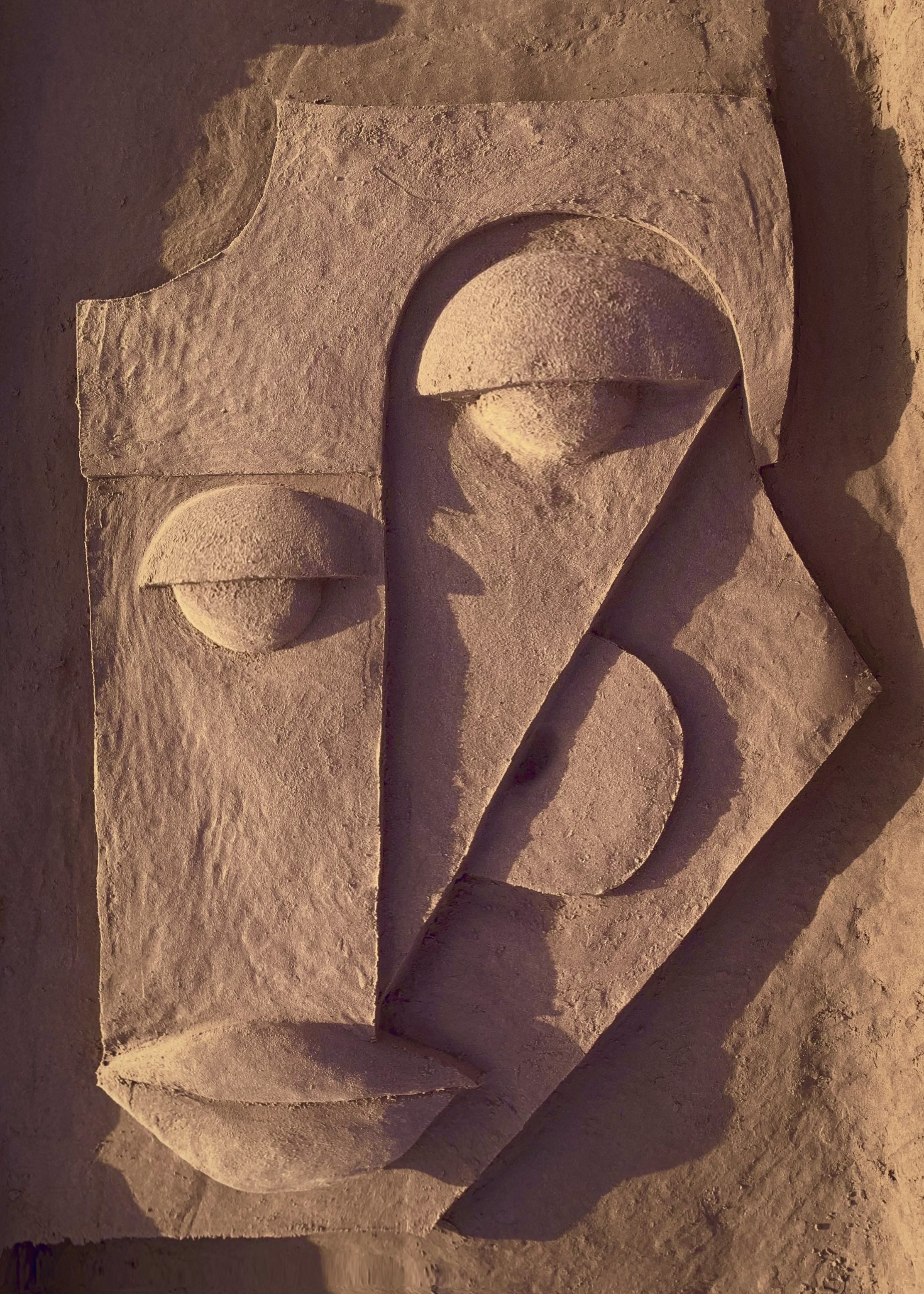 Sand bas-relief sculpture with abstract curved forms in warm orange-brown tones on beach surface